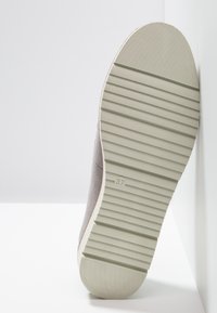 Semelle d'une chaussure gris clair avec des rainures horizontales et la taille "37" embossée au centre, positionnée verticalement contre une surface blanche.