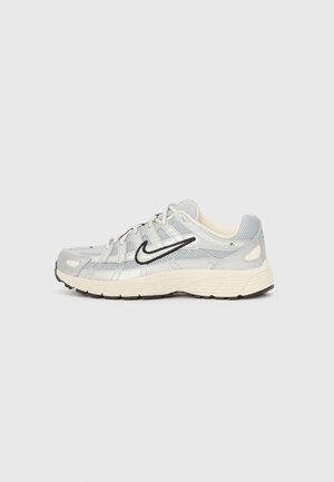 Grå idrettssko laget av mesh og syntetiske materialer, med svart Nike-logo, teksturert detaljer og en kremfarget såle.