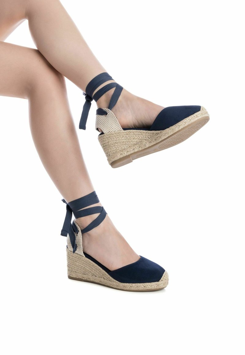 Sandalias de cuña de esparto en azul marino con suela de yute tejido y correas cruzadas en el tobillo. Diseño de punta cerrada con parte superior de tela suave.