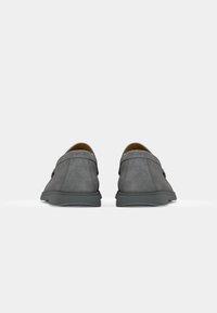 Zapatos grises de ante sin cordones con un perfil bajo, que presentan una textura suave, punta redondeada y un diseño minimalista, con un interior sutil en color marrón claro.