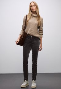 Beige stickad polotröja med ett texturerat mönster, tillsammans med mörkgrå slim fit-byxor och ljusa sneakers. Brun axelväska.