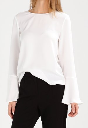 Blusa bianca a maniche lunghe realizzata in tessuto leggero e morbido. Presenta un collo a barca e maniche svasate, abbinata a pantaloni neri.
