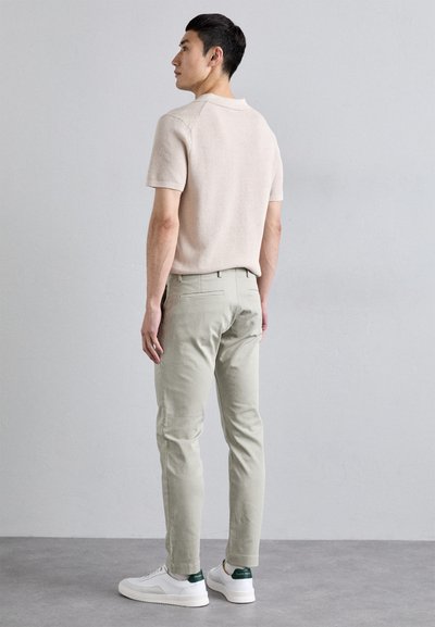 Ljust beige stickad polo, ljusgröna chinos, vita sneakers med gröna accenter. Slät textur och skräddarsydd passform.