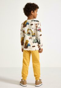 Langærmet skjorte i cremefarve med farverige tryk af entreprenørmaskiner, kombineret med gule joggingbukser, der har en afslappet pasform og manchetter ved anklerne.