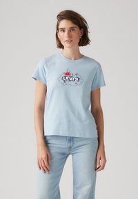 T-shirt in cotone azzurro chiaro con maniche corte, caratterizzato da una stampa grafica di una mela rossa e fiori, con il testo "LEVI'S" in design di nuvole.