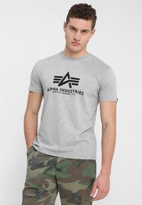 Grå bomulds t-shirt med et sort grafisk logo med vinklet design, parret med camouflage cargo bukser. Korte ærmer og rund halsudskæring.