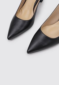 Stilettos negros de punta afilada con un upper de cuero liso y una plantilla en contraste de color beige, que presentan un diseño minimalista y una silueta elegante.