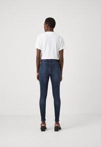 Jeans oscuros y ajustados de cintura alta, combinados con una camiseta blanca de manga corta. Textura de denim suave y detalles de bolsillos mínimos.