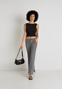 Top ajustado preto, calças largas listradas em preto e branco, mala de ombro preta e sandálias rasas. Modelo em pé contra um fundo branco.