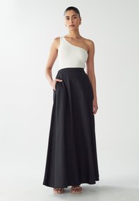 Top bianco a coste con una spalla sola abbinato a una lunga gonna nera fluida con tasche. L'outfit ha una texture liscia ed è elegante nel design.