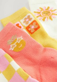 Drei Paare von bunten Baumwollsocken: pink mit einem Sonnengrafik, gelb mit Blumenmustern und weiß mit einem Sonnendesign.