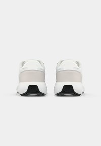 Un paio di sneakers bianche e grigie chiaro viste da dietro, con suole bianche spesse e dettagli neri sulla parte inferiore.