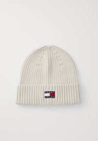 White knit beanie with a ribbed texture, featuring a small "TOMMY JEANS" logo patch in blue, red, and white on the folded cuff.