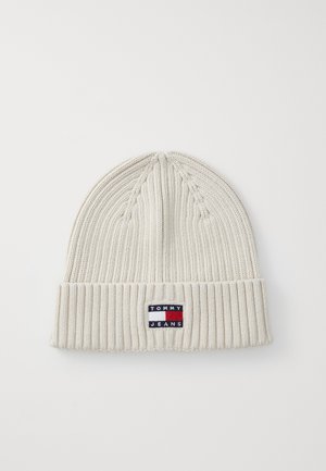 White knit beanie with a ribbed texture, featuring a small "TOMMY JEANS" logo patch in blue, red, and white on the folded cuff.