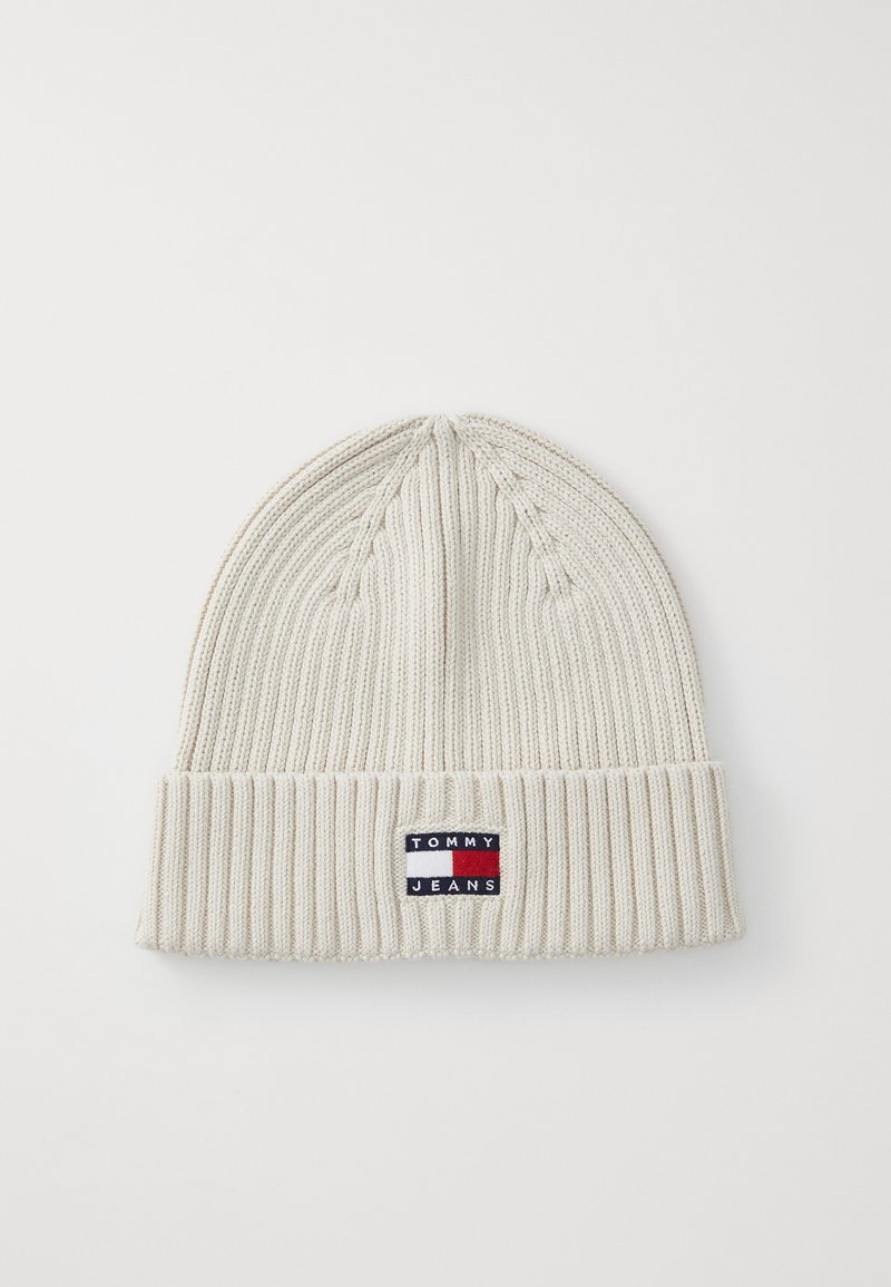 White knit beanie with a ribbed texture, featuring a small "TOMMY JEANS" logo patch in blue, red, and white on the folded cuff.