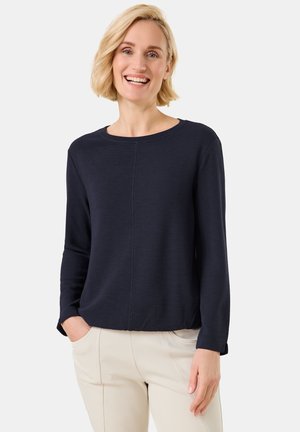 Dunkelblaues Langarmshirt mit Rundhalsausschnitt, strukturiertem Stoff und Nahtdetails. Kombiniert mit hellen Hosen.