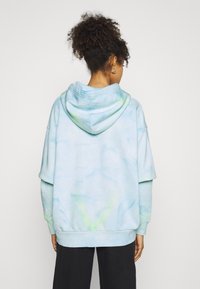 Yli-iso huppari vaaleansinisessä tie-dye-kuosissa, jossa on pehmeä rakenne. Mukana tilava huppu sekä ribbaustekstiili hihansuissa ja helmassa.