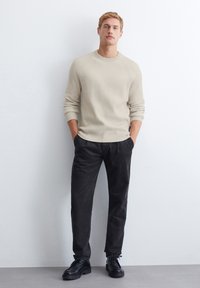 Beige ribattu paita, jossa on pyöreä kaula-aukko, yhdistettynä tummanharmaisiin laskostettuihin housuihin ja mustiin nauhakenkiin. Yksinkertainen ja moderni muotoilu.