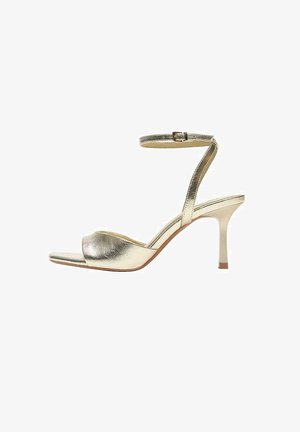 Sandale metalizată aurie cu toc înalt, bareta la gleznă, vârf decupat și toc subțire de 7 cm pe fundal alb.