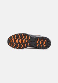 Semelle de chaussure de trail running New Balance noire et orange montrant un motif de crampons profond et multidirectionnel pour une bonne traction sur diverses surfaces.