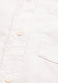 White cotton shirt with a placket, featuring soft texture, four round buttons, and a front pocket on the left side.