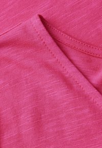 Růžová látka s hladkým povrchem, s mírně melírovaným vzorem a zakřiveným švem kolem výstřihu. Bez viditelných kovových částí či akcentů.