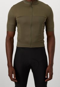 Maillot de cyclisme vert olive à manches courtes, col montant et fermeture éclair intégrale à l'avant ; accompagné de cuissards de cyclisme noirs rembourrés.