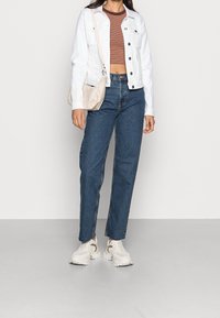 Vit denimjacka, randig brun crop top, blåa högmidjade jeans, beige väska och kraftiga vita sneakers med texturerade detaljer.