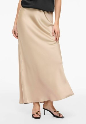 Jupe midi en satin beige avec des sandales à talons noires à brides fines, avec un accent doré, portée avec un top noir.