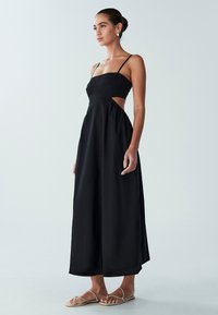 Must maxi-kleit õhukeste rihmade, vormitud bodi ja väljaulatuvate külgedega, millel on voogav seelik ja sile tekstuur.