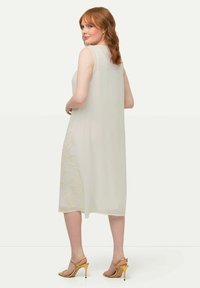 Vestido ligero sin mangas en marfil transparente con bordado floral en el costado. Combinado con tacones dorados de tiras. Textura suave y de longitud media.
