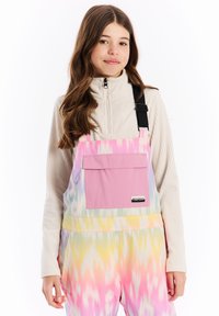 Farebný overal s motívom tie-dye v odtieňoch ružovej, žltej a pastelových farbách, s prednou vreckom a nastaviteľnými čiernymi ramienkami. Textúrovaný rebrovaný vrch.
