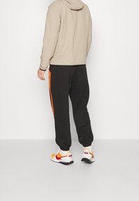 Beige textured hoodie with a hood, paired with black sweatpants featuring an orange side stripe and white, red, and yellow sneakers.