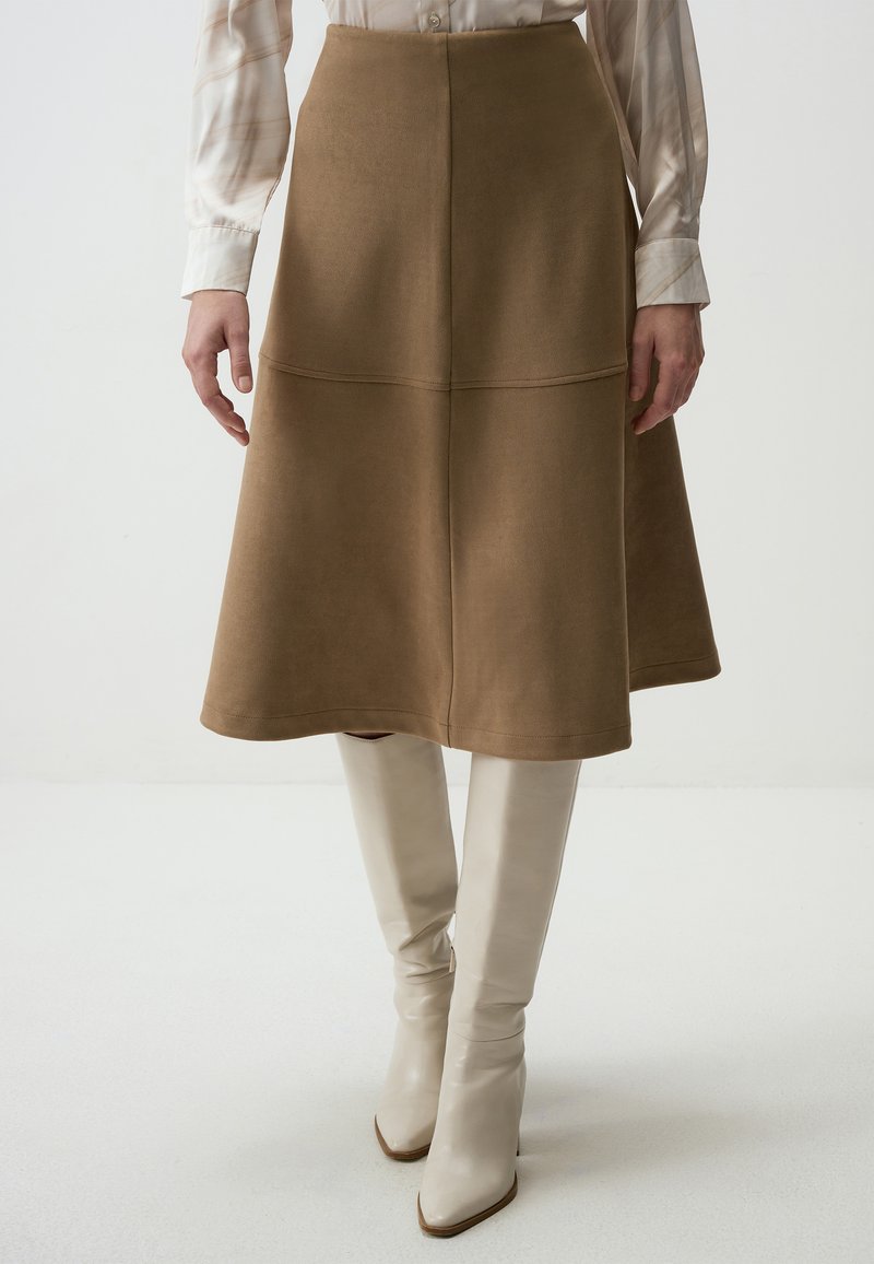 Jupe midi en suede marron avec une forme évasée, dotée de coutures et d'une taille haute. Associée à des bottes à talons beiges clairs arrivant jusqu'aux genoux.