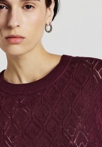 Maglione a maglia bordeaux con un motivo a diamante traforato, con colletto rotondo a coste e dettagli in tessuto testurizzato.