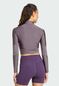 Långärmad, ljuslila träningströja med en figurnära design och hög krage, i kombination med högmidjade, mörklila shorts. Slät textur.