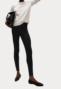 Svarta leggings i stretchigt material, ihopparade med en ljusgrå tröja och svarta platta skor. Outfiten inkluderar en svart handväska.