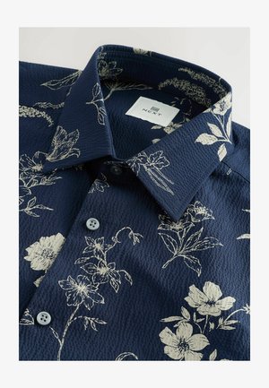Navy floral shirt featuring a textured fabric, light beige floral pattern, two buttons, and a classic collar with a branded label inside.