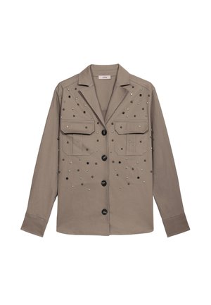 Giacca camicia oversize color khaki con due tasche frontali, caratterizzata da borchie metalliche di diverse dimensioni disposte decorativamente, rifinita con bottoni neri.