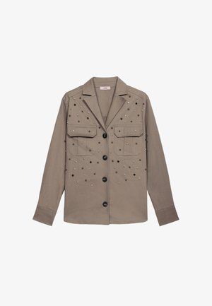 Khakifarbenes, übergroßes Hemd-Jacke mit zwei vorderen Taschen, verziert mit dekorativ angeordneten, metallischen Nieten in verschiedenen Größen, und mit schwarzen Knöpfen abgeschlossen.