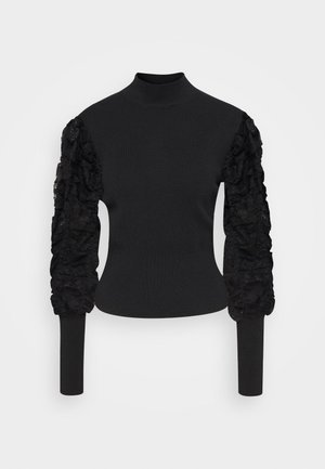 Zwarte trui met een hoge hals. Getailleerd lijfje en lange mouwen, met een gestructureerde, gerimpelde kanten inzet aan de linkermouw.