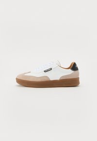 Sneaker in suede bianco e tan con suola in gomma marrone, lacci piatti e accentuazione nera sul tallone. Presenta un dettaglio con il logo sul lato.