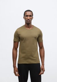 Olivovo zelené bavlnené tričko s krátkymi rukávmi a okrúhlym výstrihom. Na ľavej strane hrudníka je malý čierny logotyp, hladká textúra.