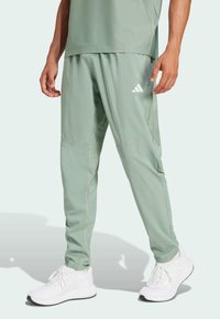 Světle zelené sportovní kalhoty s volnějším střihem, vyrobené z hladkého, lehkého materiálu. Obsahují logo Adidas a boční kapsy.