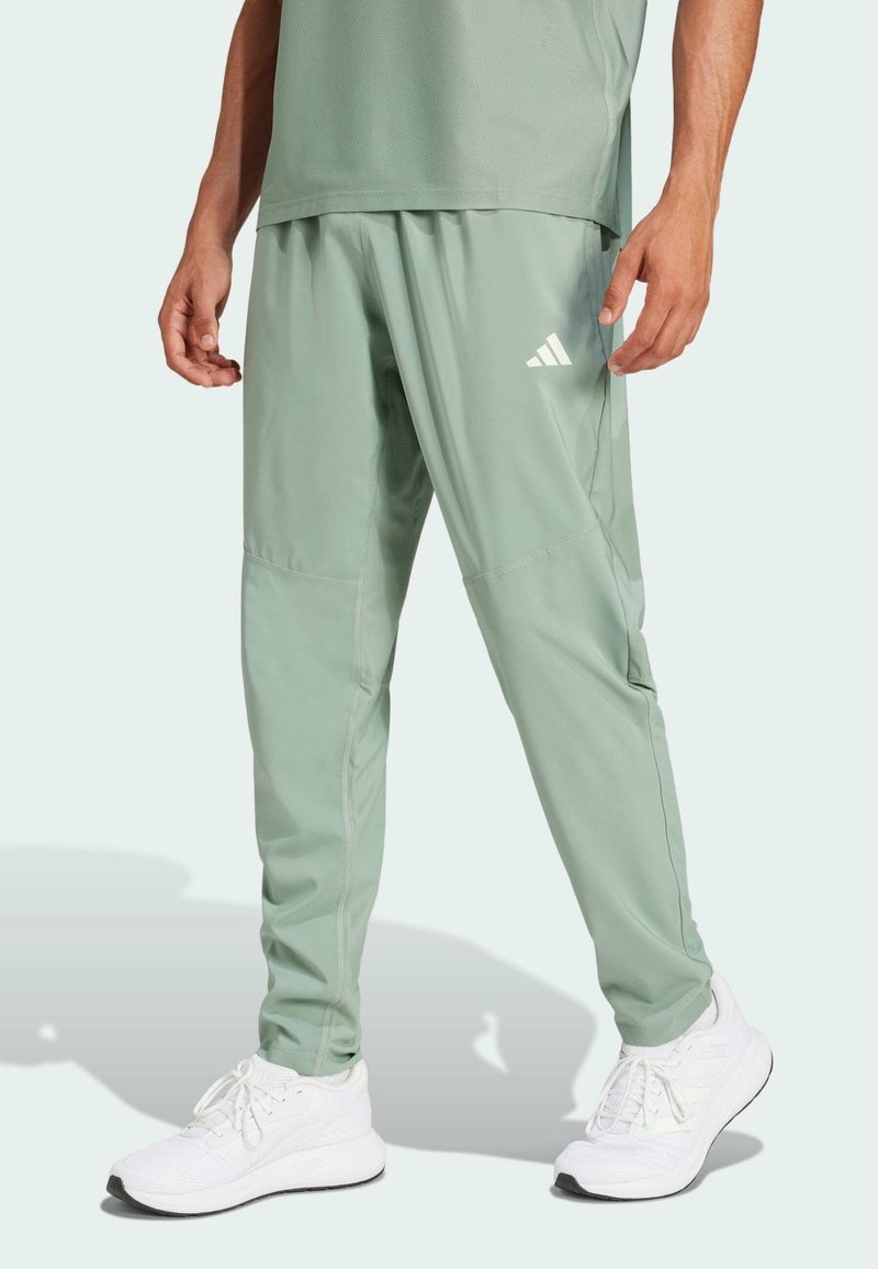 Světle zelené sportovní kalhoty s volnějším střihem, vyrobené z hladkého, lehkého materiálu. Obsahují logo Adidas a boční kapsy.