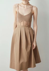 Beige geribbelde lijfje met doorschijnende inzetstukken, gecombineerd met een geplooide A-lijn rok in een bijpassende beige tint, voorzien van een gladde textuur en een strik aan de zijkant.