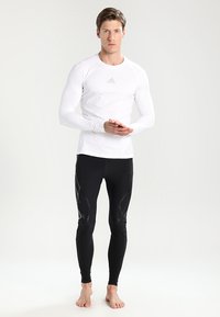 Balta garām piedurknēm sporta krekls un melnas legingas ar teksta akcentiem un pieguļošu piegriezumu, uz krekla priekšpuses ir logos.