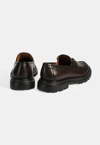 Braune Lederschuhe mit einem flachen Design, ausgestattet mit einer strukturierten schwarzen Gummisohle und einem dezenten Akzentriemen über dem Vorderfuß.