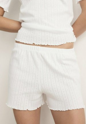 Frau trägt weißes kurzärmeliges, geripptes Oberteil und passende Shorts mit elastischem Bund, dezentem vertikalem Streifen- und Lochmuster.