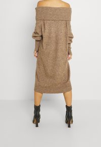 Strickkleid mit schulterfreiem Design in einem gedämpften Braunton, ausgestattet mit langen Ärmeln, gerippten Bündchen und einem taillierten Saum. Kombiniert mit schwarzen Knöchelstiefeln.